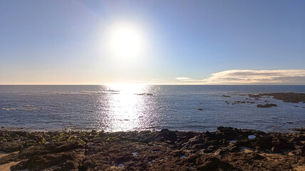 The ocean shore. The sun is shining brightly in the blue sky over the ocean. Horizontal image.