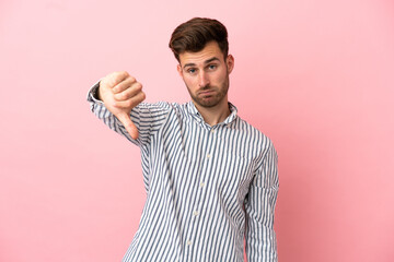 Young caucasian handsome man isolated on pink background showing thumb down with negative expression