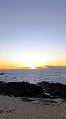 The ocean shore. The sun is sinking below the horizon in a blue sky. Beautiful sunset. Vertical image.