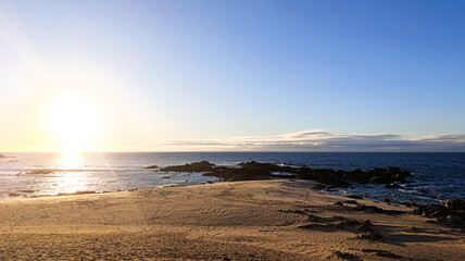 The ocean shore. The sun is sinking below the horizon in a blue sky. Beautiful sunset.