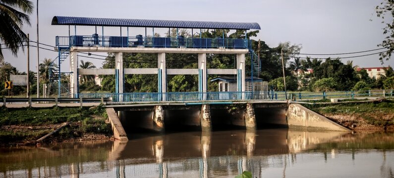 Real Water Control Flood Gate with Blue Railings and Reflection on a Calm River