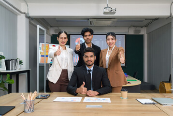 Team of successful business people gather around a table raise finger thumb up with a smile. Concept of leadership.