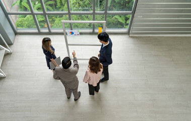 A professional man and woman stand together, engaged in a brainstorming session, using document and colorful paper notes on a transparent glass wall.