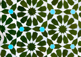 A detailed Islamic geometric mosaic featuring vibrant colors and symmetrical patterns. The design showcases traditional arabesque motifs with star shapes and interwoven lines
