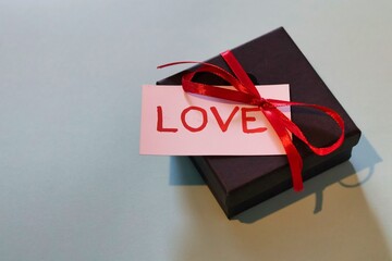 A black box with a red ribbon and a white card with the word 'love' written on it; An expression of love