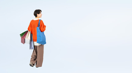 ショッピングバッグを持って歩くおしゃれなミドル女性の後ろ姿の全身写真