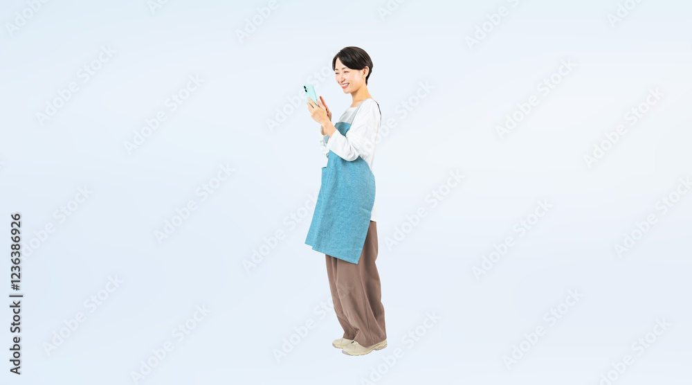 Aufkleber 笑顔でスマホを使うエプロンをつけたミドル女性の全身写真