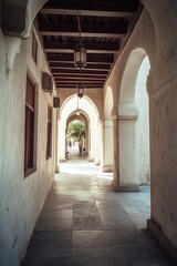 Fototapeta premium An empty stone paved pathway between two buildings, featuring arched doorways and a shaded alleyway.