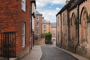 Fototapeta premium Cobblestone street winding through the historic old town of Durham, England with traditional architecture and a peaceful atmosphere.