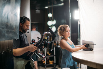 Director of photography with a camera in his hands on the set. Professional videographer at work on filming a movie, commercial or TV series. Filming process indoors, studio