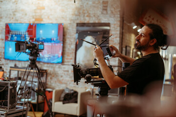 Director of photography with a camera in his hands on the set. Professional videographer at work on filming a movie, commercial or TV series. Filming process indoors, studio