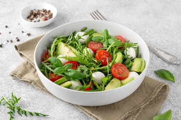 Fresh salad with arugula, mozzarella, tomatoes and avocado in a bowl. Healthy vegetarian dish.
