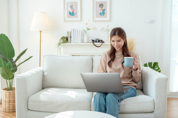 Young Woman Enjoys Working on a Laptop While Sipping Coffee in a Cozy Living Room Setting