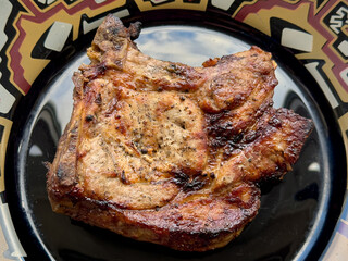 Delicious piece of fried meat beautifully presented on a black plate with a vibrant pattern. The meat appears browned and juicy.