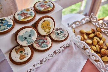 Cookies with colorful animal designs white icing tiered stand tray small round pastries pink tablecloth.