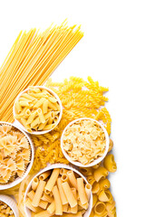 A variety of types of dry pasta in white ceramic bowls surrounded by crumbled pasta on a white background. pasta of different shapes: bows (farfalle), feathers (penne), spirals (fusilli), tubes 