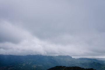 Aerial view of mist-covered mountains and valleys under a dramatic overcast sky, creating a serene and atmospheric rural landscape.