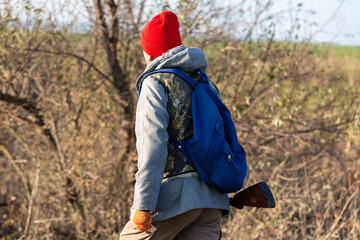 Mature hunter man holding a shotgun and walking through a field