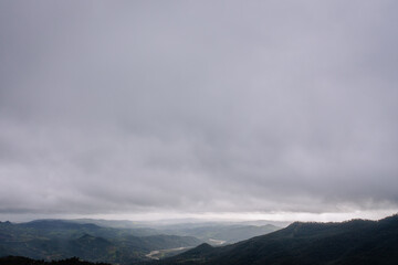 Aerial view of misty green valleys, rolling hills, and distant mountains under an expansive cloudy...