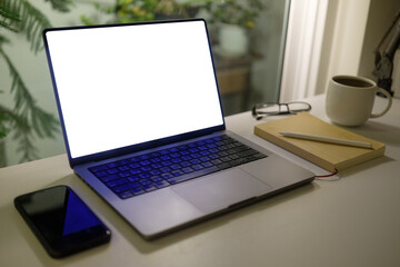 Fototapeta premium Cozy workspace with laptop displaying a blank screen, notebook, coffee cup and glasses, for portraying productivity and creativity during quiet hours.