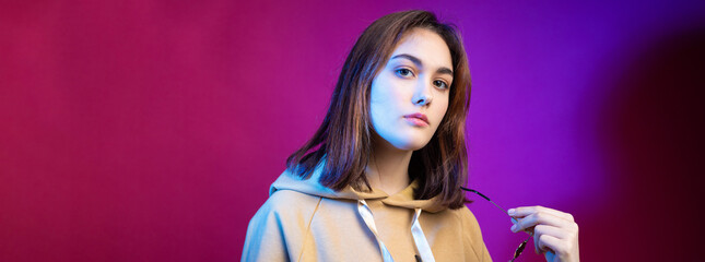 Portrait of a woman in a hoodie, with beautiful makeup on a purple trendy background in the studio.