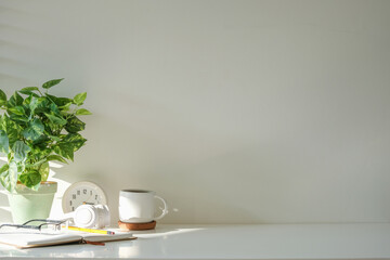 Comfortable workspace arrangement of a potted plant, notebook, a coffee mug and a clock.