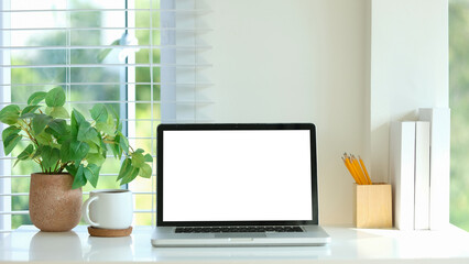Minimalist desk laptop with a blank white screen, coffee mug, and a lush green plant.