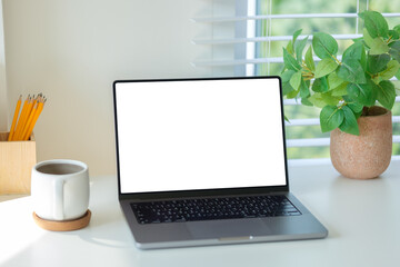 Fototapeta premium Laptop with empty screen, coffee a wooden pencil holder, and a lush green plant against a window with blinds.