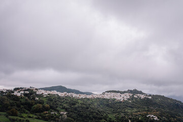  A distant view of a white village on a green hillside under a cloudy sky, surrounded by lush vegetation and rolling terrain.