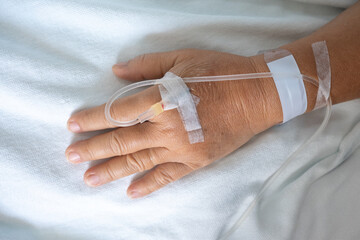 Hand of patient lying on bed in ward at hospital with saline solution tube injection and sterile plaster bandage on hand