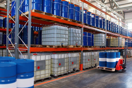 Chemical warehouse. Barrels with flammability symbol. Forklift in warehouse area. Oil barrels are stored on racks. Warehouse hangar inside. Interior industrial chemical storage facility. 