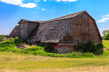 A large, old barn with a slanted roof sits in a field