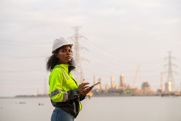 Engineers wearing safety gear, including hard hats examining survey standing industrial facility gas or oil refinery engaged in a job requires high safety standards concept.	