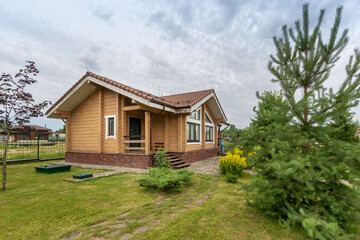 A wooden house made of timber with a tiled roof, on a green lawn with flowers and fir trees.