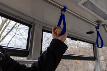 hand holding a blue strap in public bus interior, with windows showing a view of trees and winter...