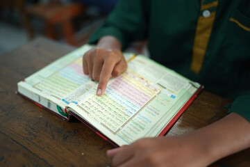 Malang,Indonesia - ‎July 13,2023: The fingers of Asian children read the Quran or the Holy Book of Muslims who have studied the Quran since an early age. Muslim activities during the month of Ramadan.