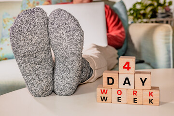 4 day work week symbol. desk with wooden blocks with words 4 day work week. Person working with laptop on lap and feet on table. Remote work. Business concept, change from 5 to 4 day work week