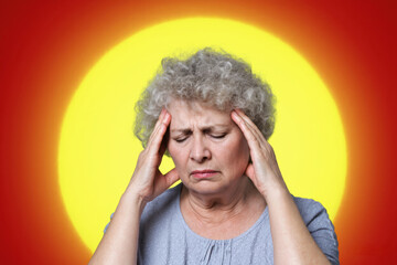 Portrait of an elderly woman  and curlers holding her head and wincing from a headache, against the background of a large sun with solar flares and swirls of solar radiation