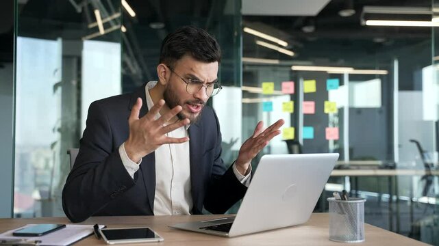 Angry businessman arguing talking on video call using laptop in office. Excited dissatisfied executive expressing emotion of anger, discussing stressful business situation or conflict resolution