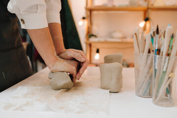 Craftswoman is preparing clay for making ceramic crockery. Female potter rolls piece of clay before sculpting.