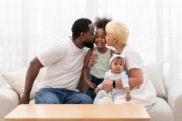 Fototapeta premium bonding black family spend free time together in the living room,father and mother embracing a daughter and kiss on cheek with affectionate