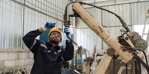 Professional male engineer maintenance automatics robotic arm in industry factory. African American male engineer repairing automatic robotic arm machines. Industry robot manufacturing technology