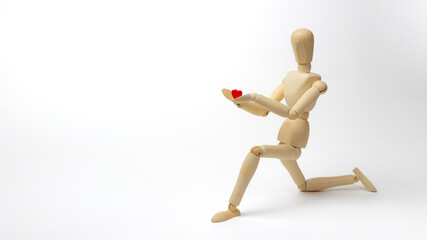 Wooden doll stands on knee and holds a red wooden heart in her hands. Valentine's Day holiday card.