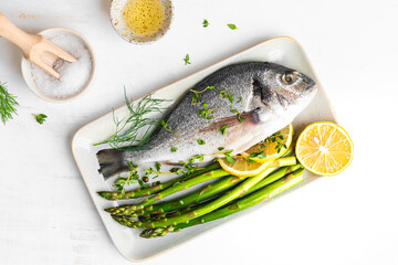 Fresh raw Dorado with asparagus spices, herbs, lemon and salt over white background.