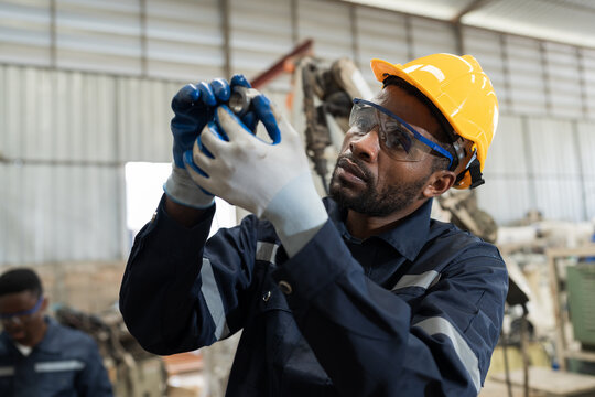 African American male engineer inspecting quality of parts of lathe machine in the industry factory. Male worker checking spare parts of machine