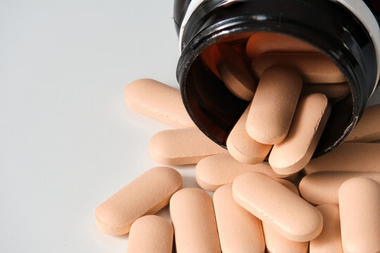 Macrophotography of pink oblong pills spilling from a dark bottle on a white surface
