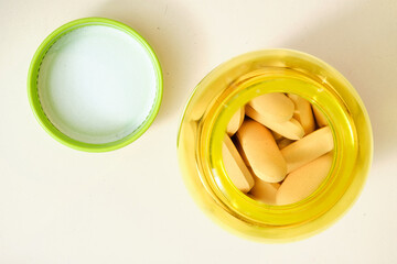 Yellow plastic bottle containing oblong pills with its green cap and foil seal removed, signifying...