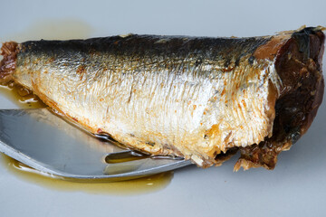Oily sardine being lifted by a fork on a white plate, ready to be eaten
