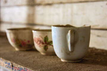 Three cups with floral designs sit on a wooden shelf