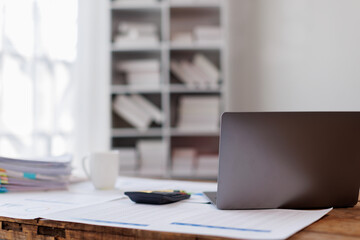Laptop Computer, notebook, and eyeglasses sitting on a desk in a large open plan office space after working hours
